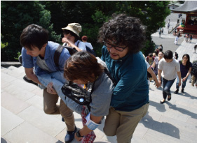 鶴岡八幡宮の階段で車椅子の同僚を抱きかかえて登る
